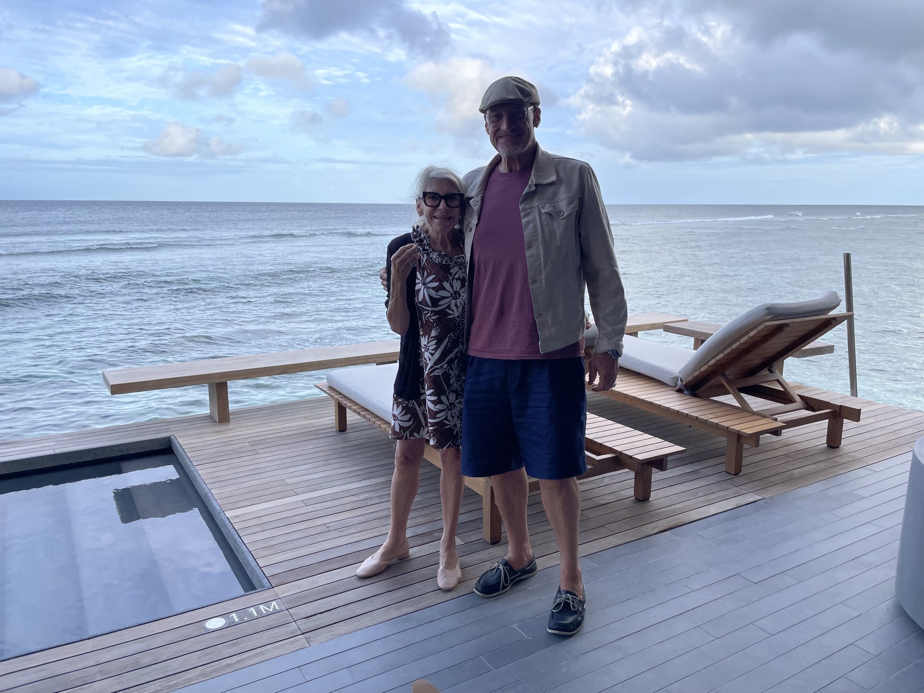 Michael by the ocean, arm around a companion, on a wooden deck above the water.